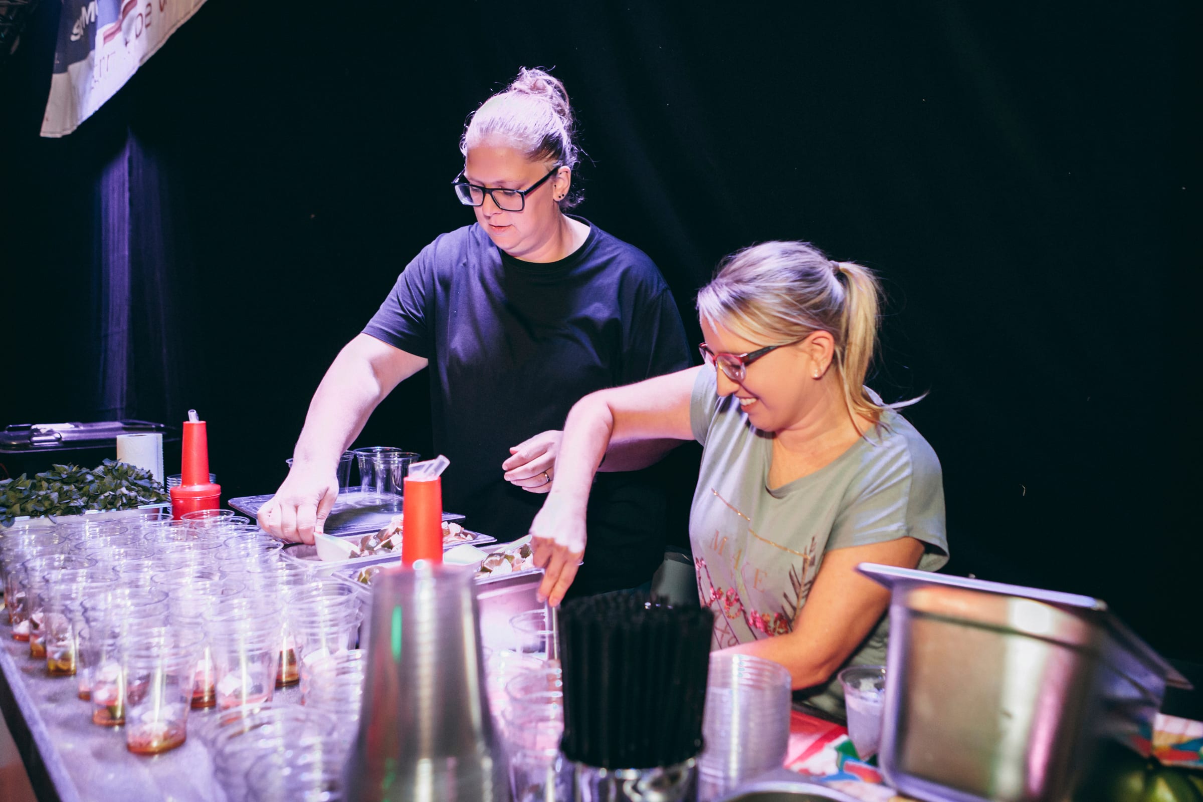 Zwei Barkeeperinnen bereiten Cocktails bei einer Firmenfeier vor, Cocktail-Becher im Vordergrund