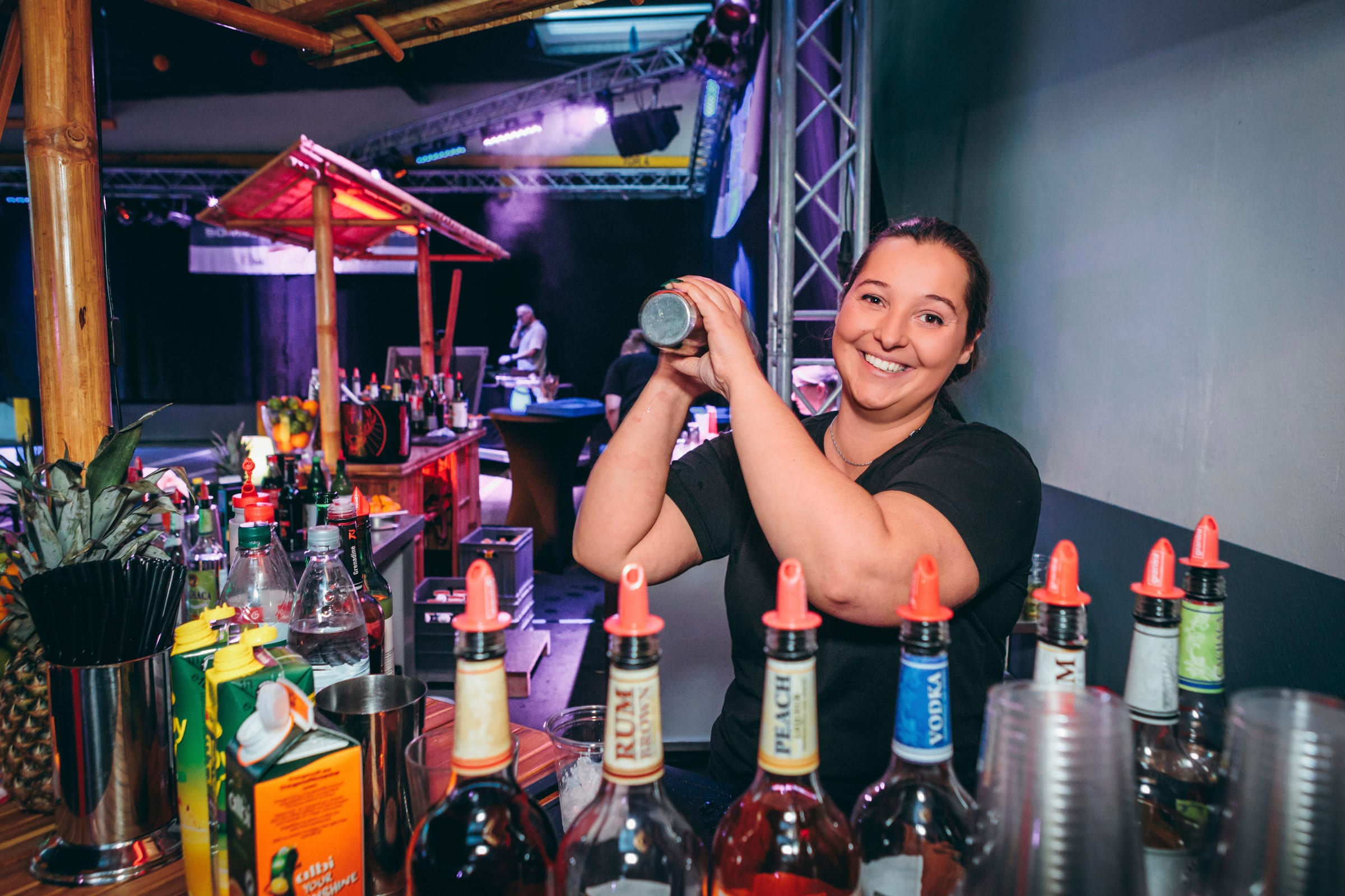 Barkeeperin schüttelt einen Cocktail bei einer Firmenfeier, Spirituosenflaschen im Vordergrund